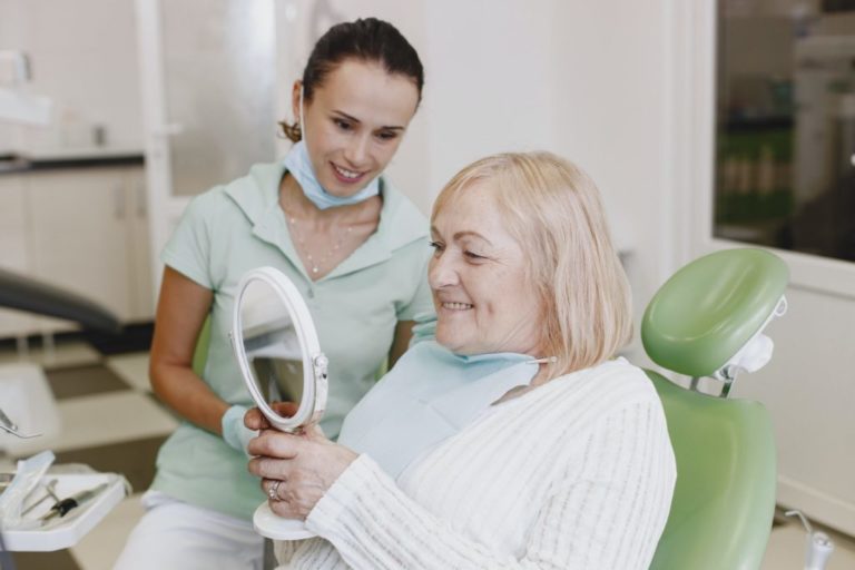 Happy patient looks at her dentures in the mirror.